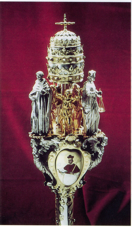 Päpstliches Zepter 1656 - Päpstliches Zepter 1656
Das Salzburger Zepterpaar gehört zu den schönsten barocken Universitätszeptern. Es kam jedoch in sehr schlechtem Zustand in Würzburg an und wurde zunächst grundlegend restauriert aber auch verändert.
Die Zepter waren 1656 geschaffen worden und sind jeweils als Zeichen der kaiserlichen und päpstlichen Privilegierung mit einer Kaiserkrone und der Tiara bekrönt. Sie waren in Würzburg so selbstverständlich in Gebrauch, dass die älteren Stifterzepter im Verlauf dieser Zeit unbemerkt abhanden kamen. Auch das Wissen um die Herkunft der neuen Zepter war verloren gegangen.
Dies sollte sich 1944 schmerzlich bemerkbar machen, als das Zepterpaar auf Druck des Gauleiters und Reichsstatthalters von Salzburg in Ausnutzung der NS-Machtstrukturen nach Salzburg zurückgebracht werden musste. Päpstliches Zepter 1656